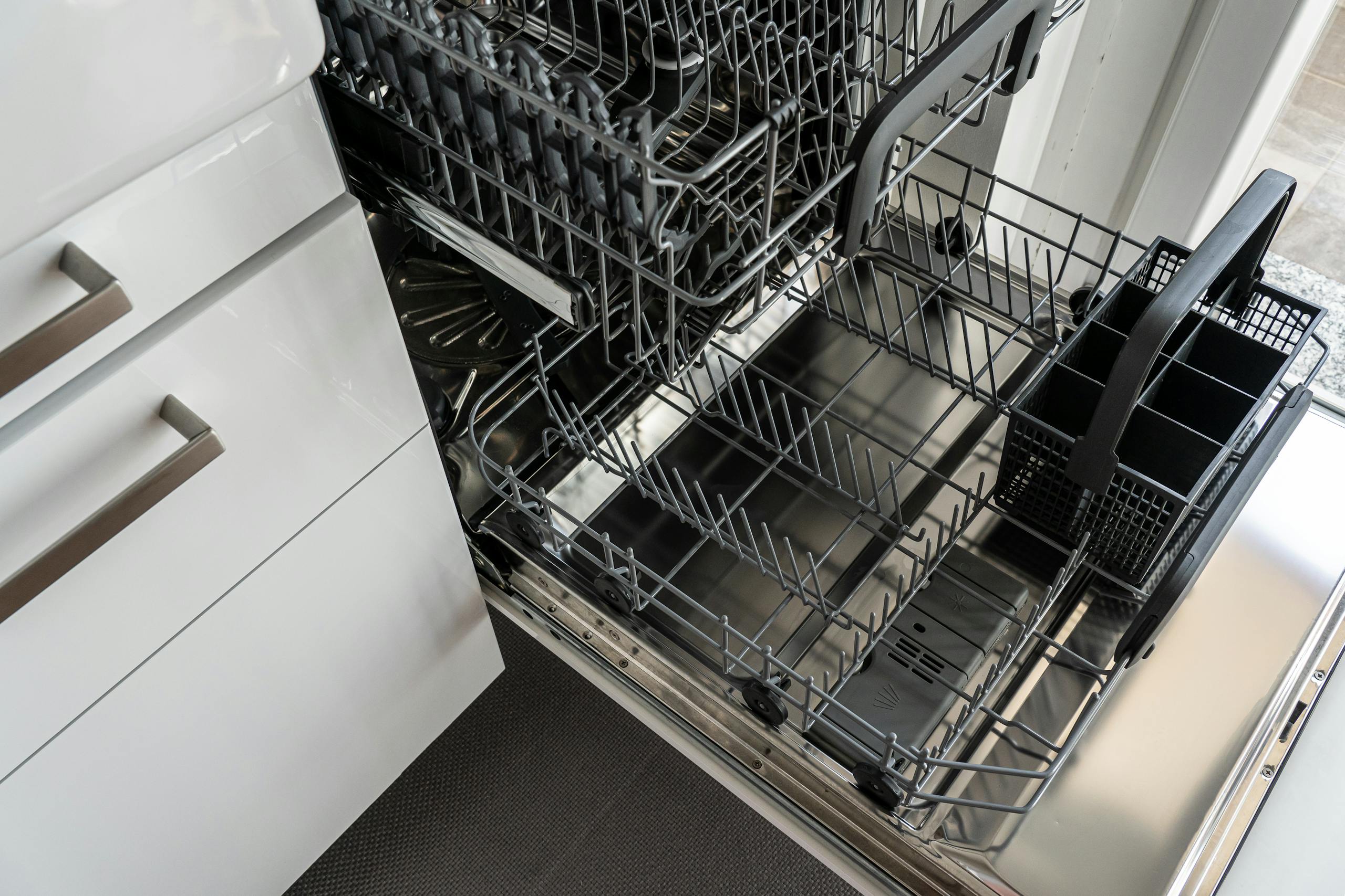 A clean and empty stainless steel dishwasher open in a modern kitchen setting.