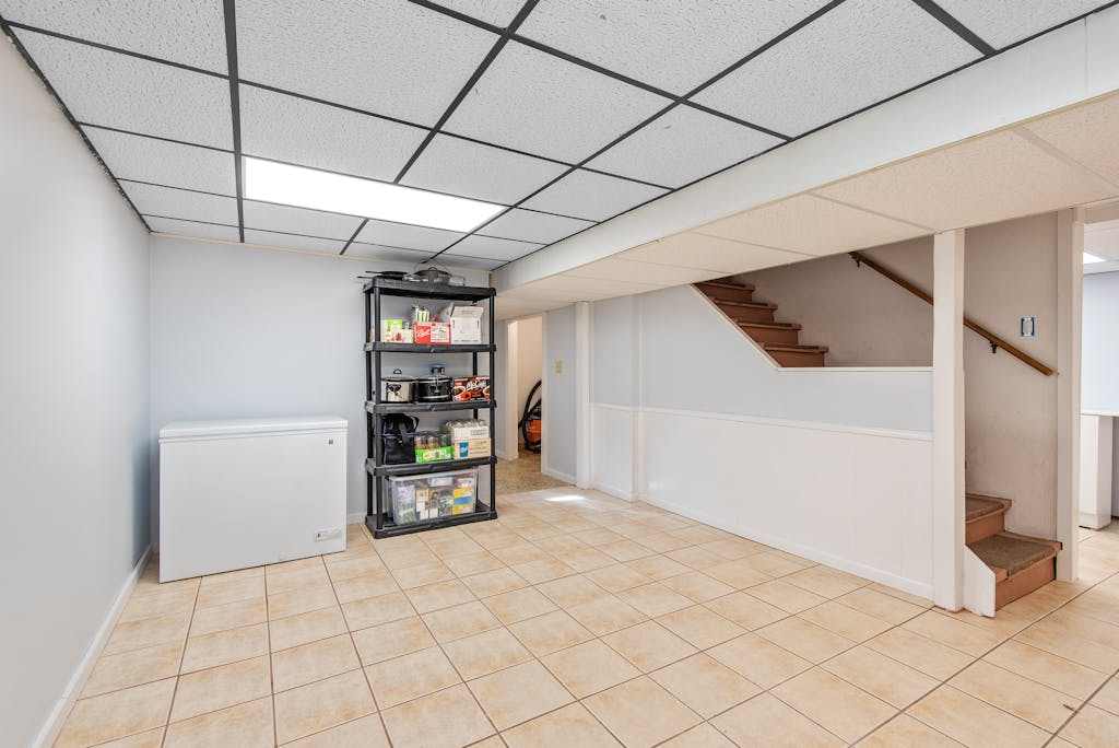 Spacious basement featuring tiled floor, storage shelves, and staircase in a modern setting.