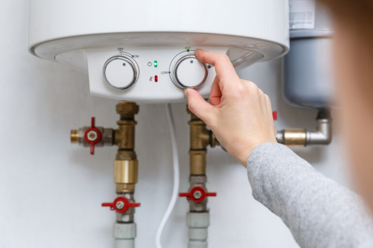 womans hand adjusts thermostat of hot water heater