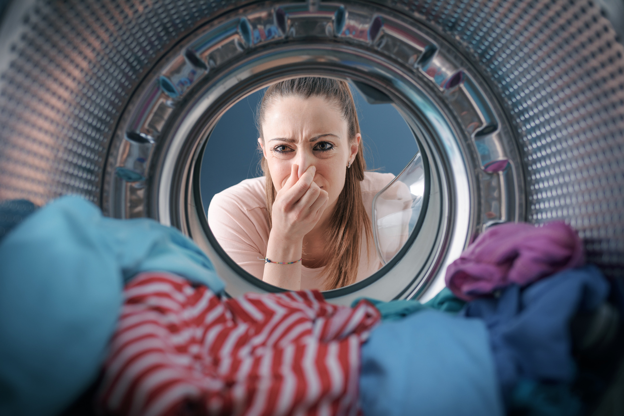 woman holding her nose looking in the washer